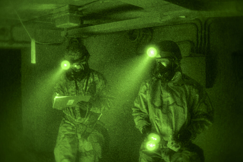 U.S. Air Force 1st Lt. Blake Janas, left, 386th Expeditionary Civil Engineering Squadron officer in charge of planning, real property and environmental compliance, and Tech. Sgt. Joe Vaughan, 386th ECES emergency management technician, inspect the interior of a simulated chemical weapons lab during a sensitive site exploitation exercise within the U.S. Central Command area of responsibility, July 24, 2025. The exercise included identifying chemical agents, documenting the scene and collecting samples under hazardous conditions. (U.S. Air Force photo by Staff Sgt. James Fritz)